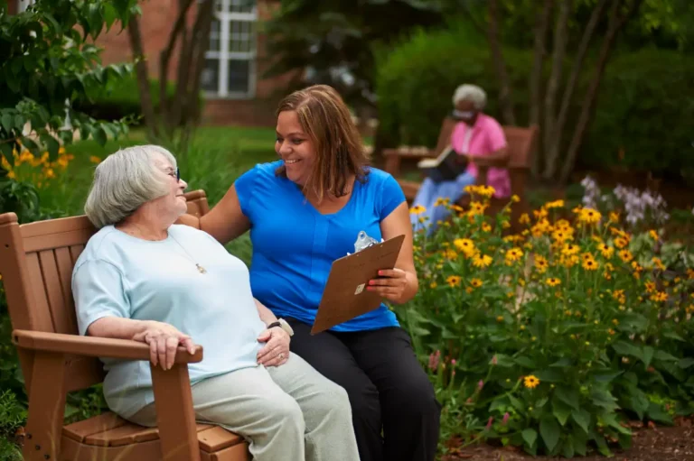 A resident talks to a Peace Village employee outdoors on a bench